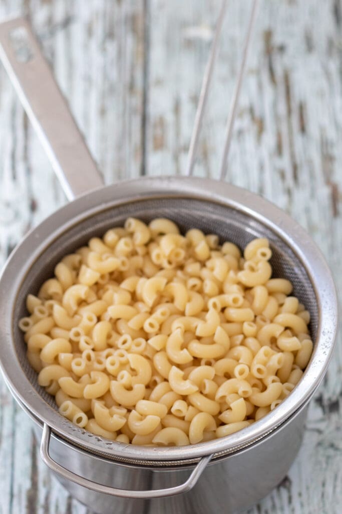 Cooked and drained macaroni sitting in a sieve over a pot.
