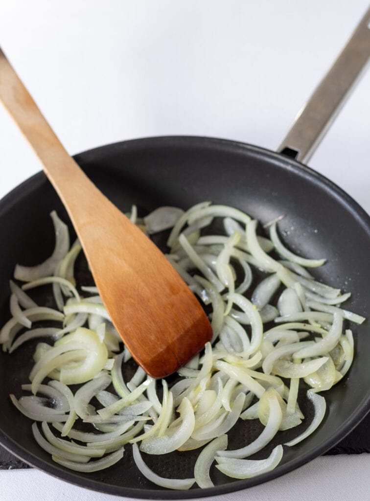 Sliced onion being sauteed in a large frying pan.