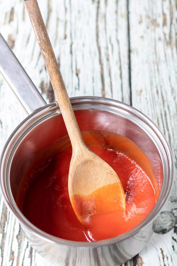 Tomato passata and tomato paste heated together in a saucepan with a wooden spoon.