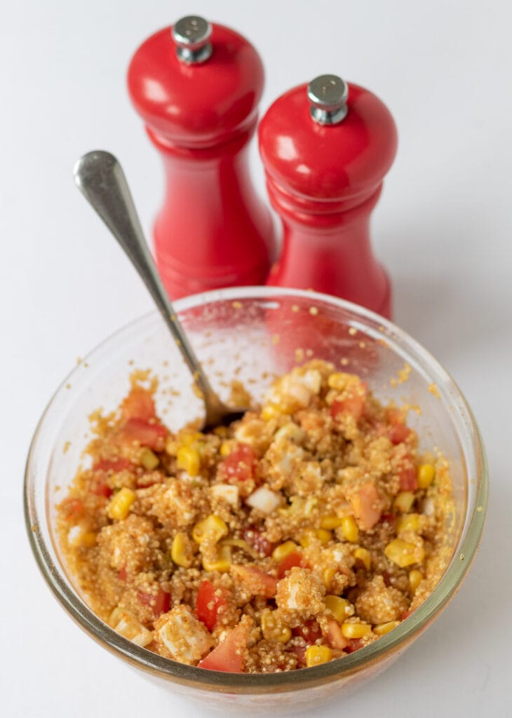 Drained quinoa in a small bowl mixed with rest of stuffed peppers ingredients.