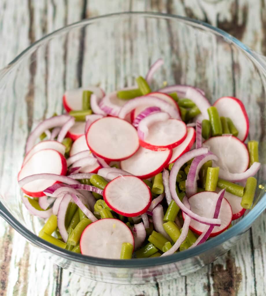 Radishes, onion and green beans in a mixing bowl.