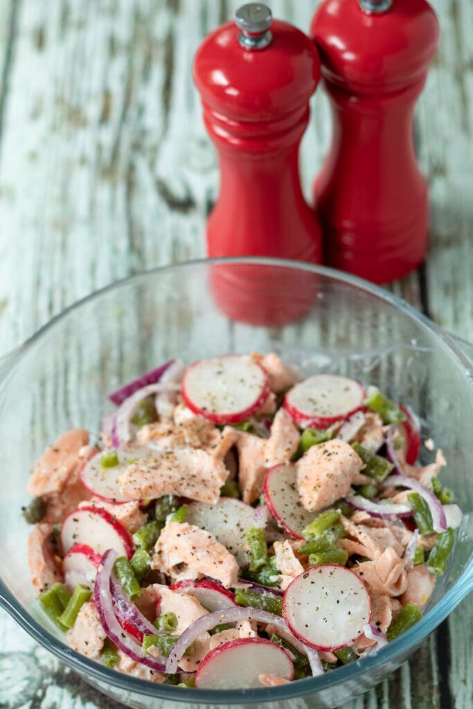 Cooked salmon added to salad ingredients and dressing and mixed together.