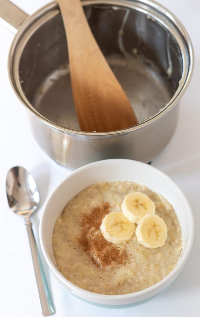Banana porridge served in a bowl. Empty saucepan with spatula in above.