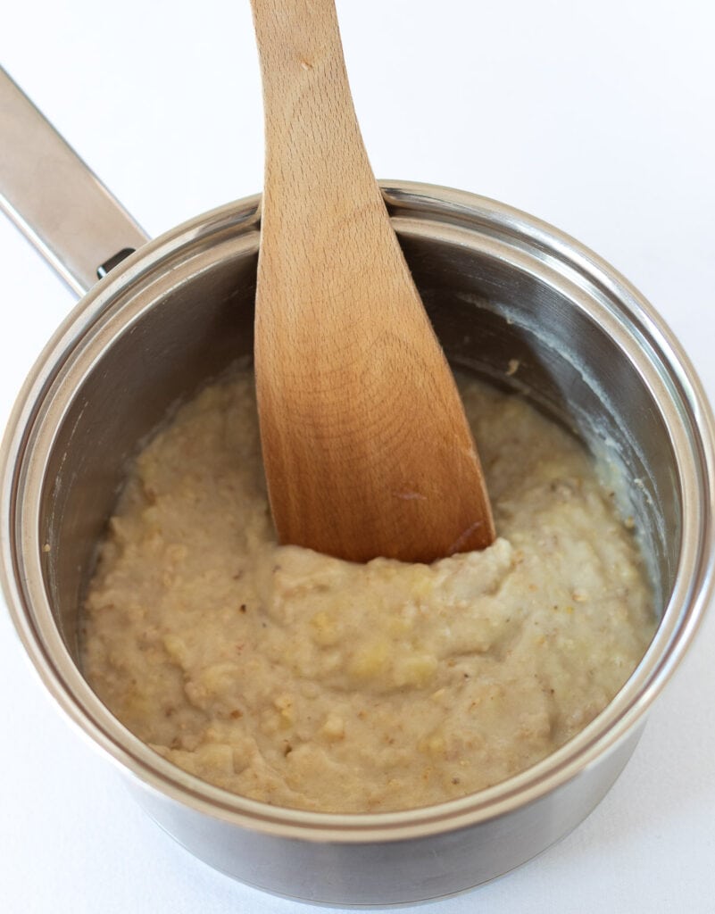 Cooked banana porridge in a saucepan with a spatula in.