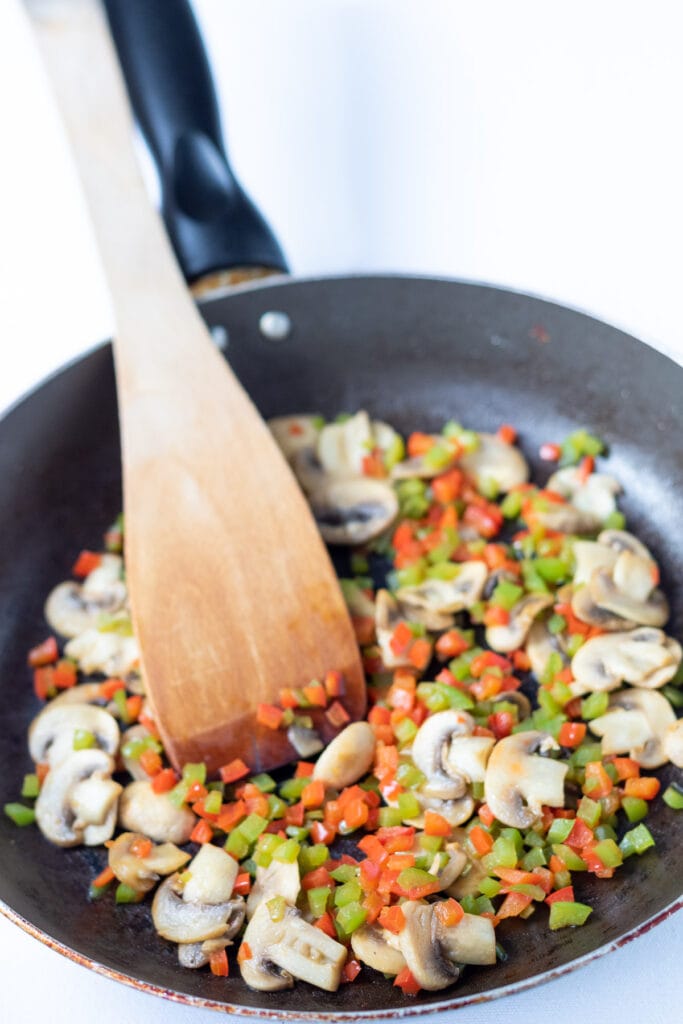 Mushrooms and diced bell peppers sauteed together in a frying pan.