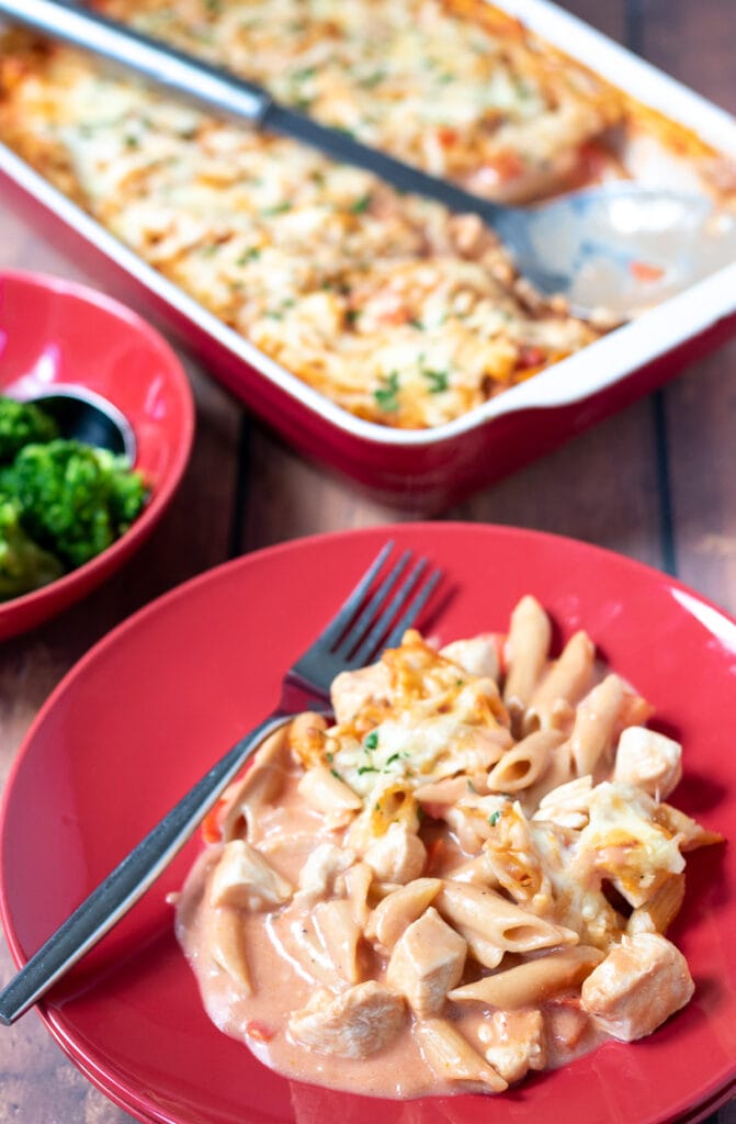 Easy creamy chicken pasta bake served on a plate. Rest of pasta bake in a casserole dish in the background.