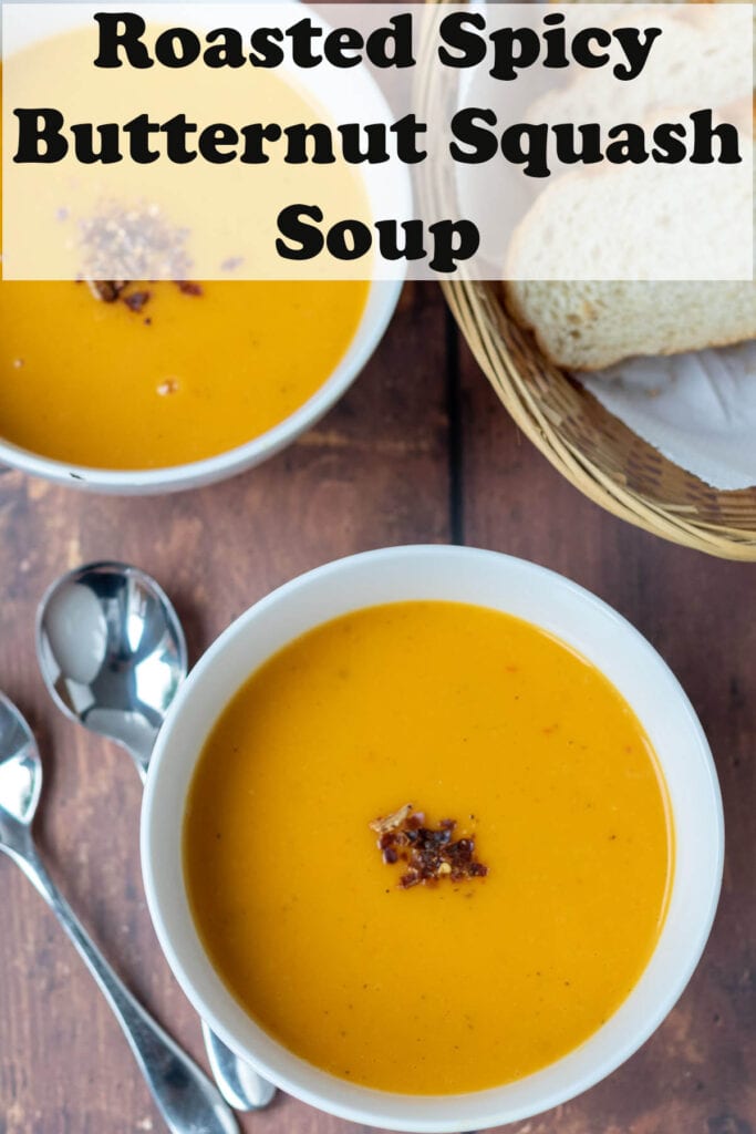Overhead view of two bowls of roasted spicy butternut squash soup garnished with dried chillies. Pin title text overlay at top.