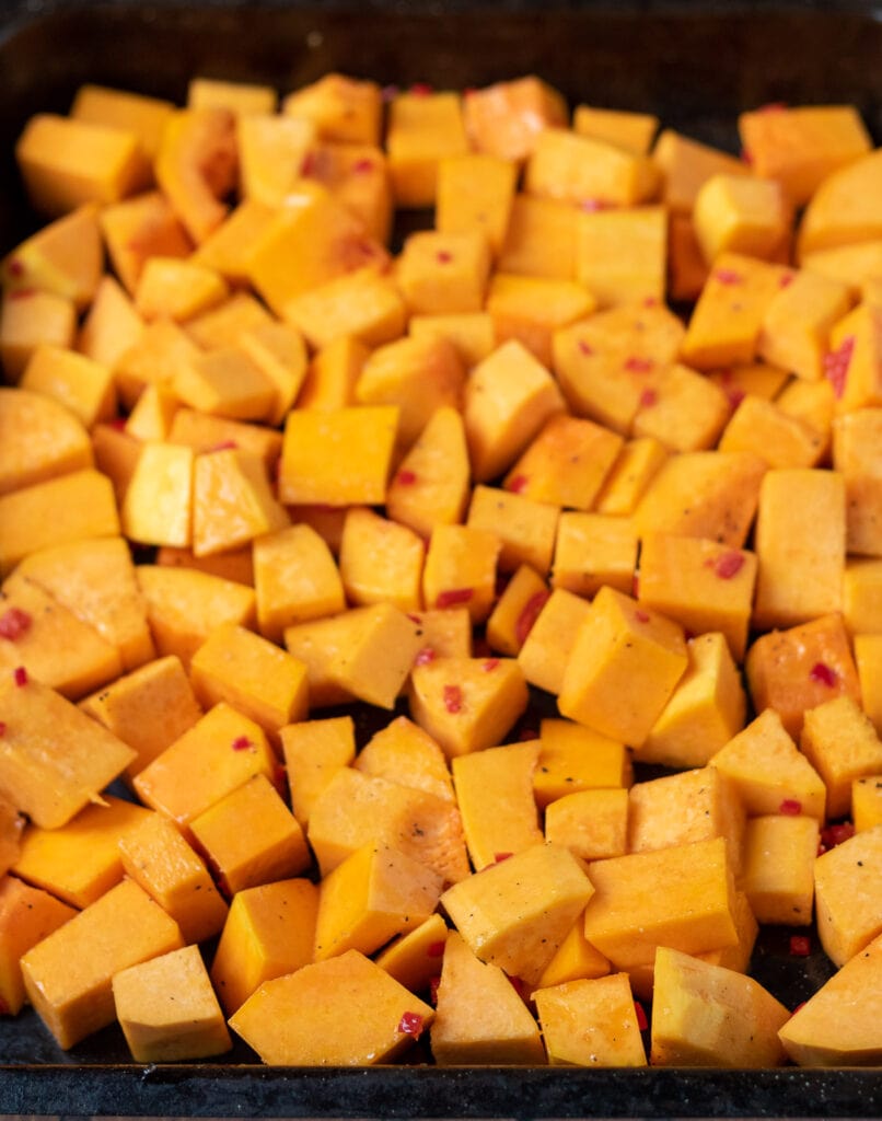 Butternut squash cubes tossed in olive oil in a roasting tray.
