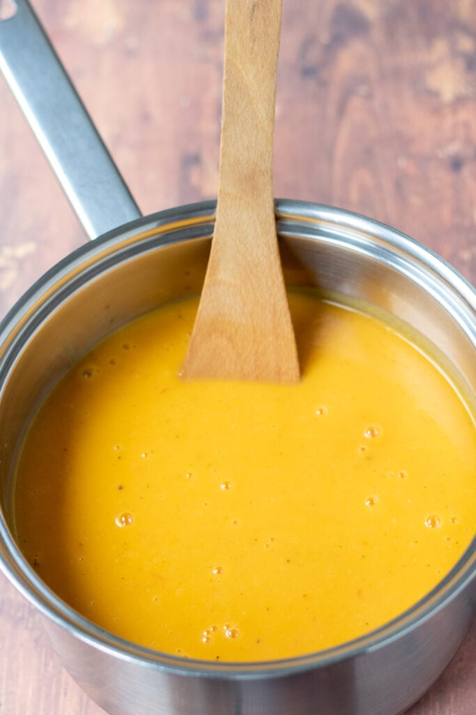 Blended roasted spicy butternut squash in a saucepan with a wooden spoon in.