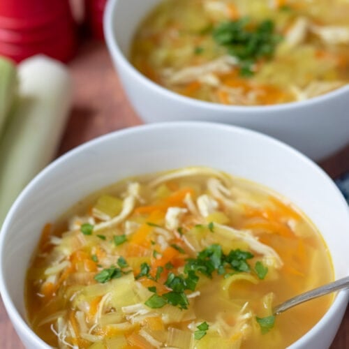 Two bowls of Scottish cock-a-leekie soup garnished with chopped parsley one in front of the other.