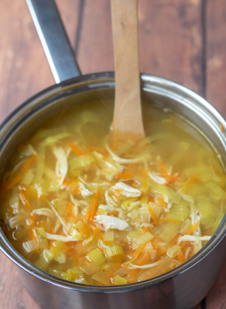 Shredded chicken breast meat stirred into soup pot of cooked grated carrot, leeks and rice.