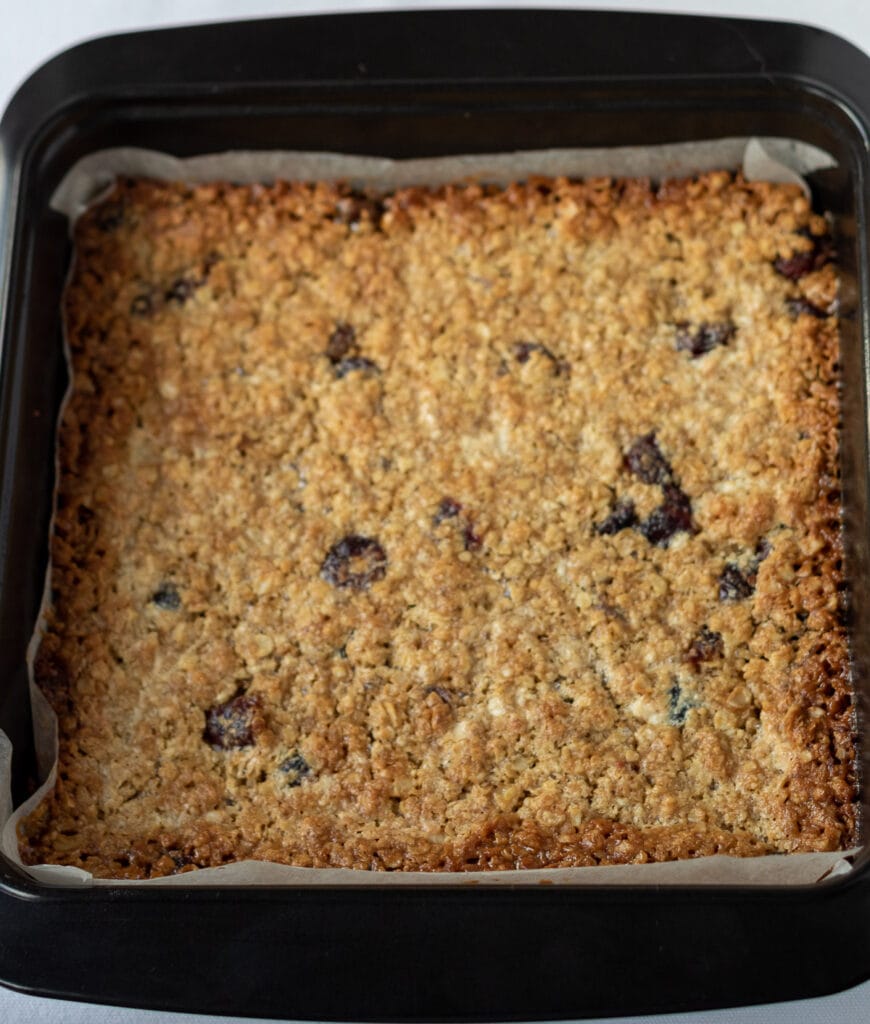 Baked cranberry and white chocolate flapjack slab in baking tin.