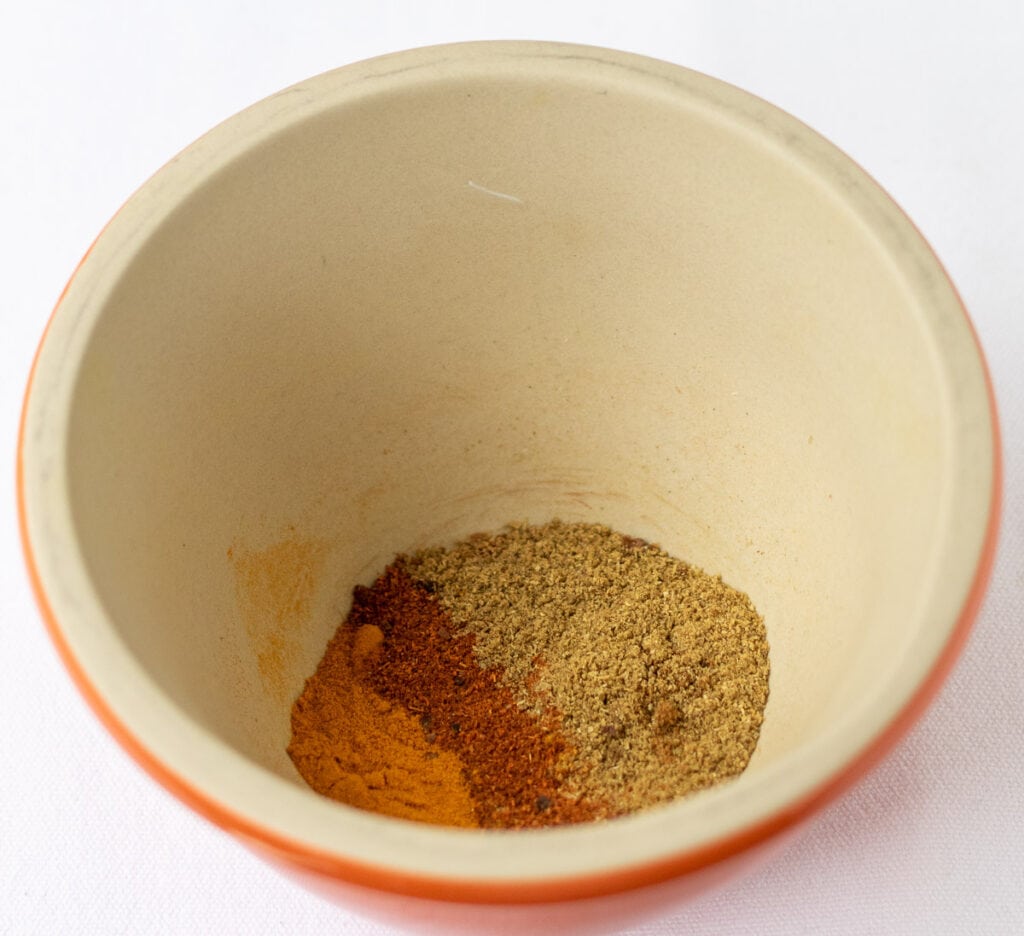 Cardomom pods, cumin, coriander, turmeric, chilli powder and clove ends crushed together in a pestle and mortar.