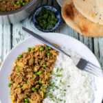Overhead view of a plate of easy lamb mince curry served with basmati rice and garnished with chopped coriander, fork to the side. Saucepan and plate of naan breads above.
