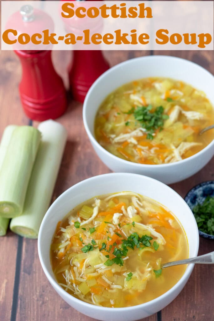 Two bowls of cock-a-leekie soup one above the other with soup spoons in. Leeks and salt and pepper cellars to the right hand side.