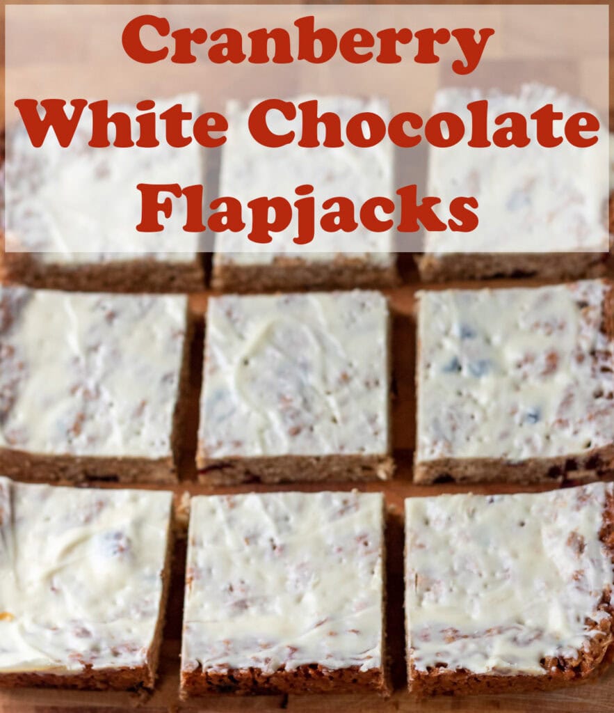 Nine cranberry and white chocolate flapjacks laid out on a wooden cutting board. Pin title text overlay at top.