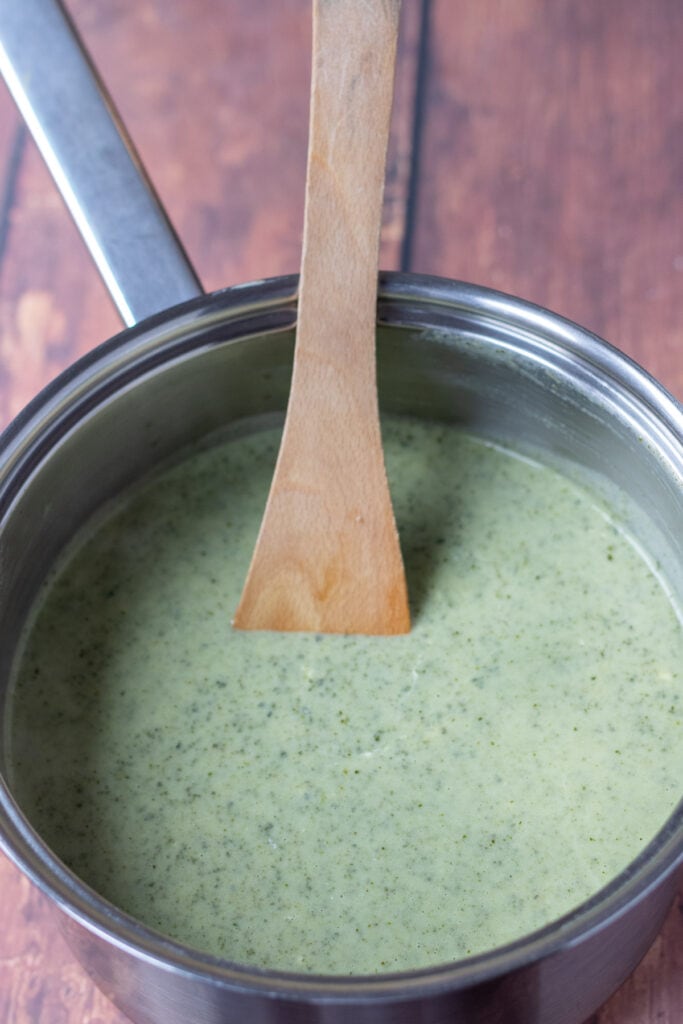 Soft cheese stirred into kale soup and combined with a wooden spoon.