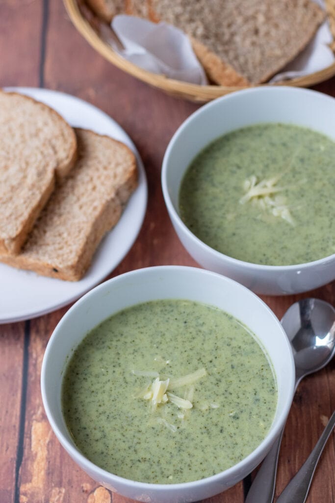 Two bowls of kale soup diagonally across from each other with slices of bread on a plate and in a bread baked alongside.