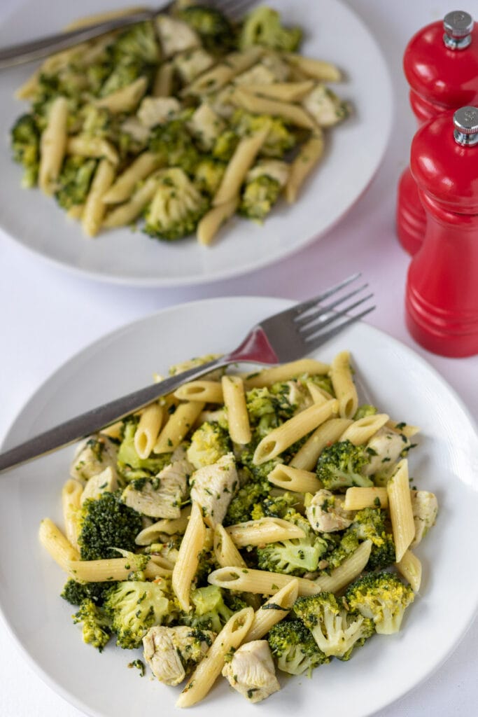 Two plates of chicken and broccoli pesto pasta with forks on. One above the other.