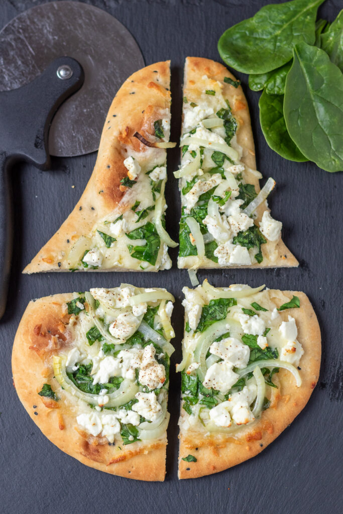 Overhead view of a spinach and feta naan pizza cut into 4 pieces.
