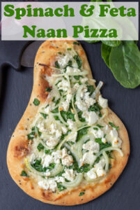 Spinach and feta naan pizza on a black slate. Pin title text overlay at top.