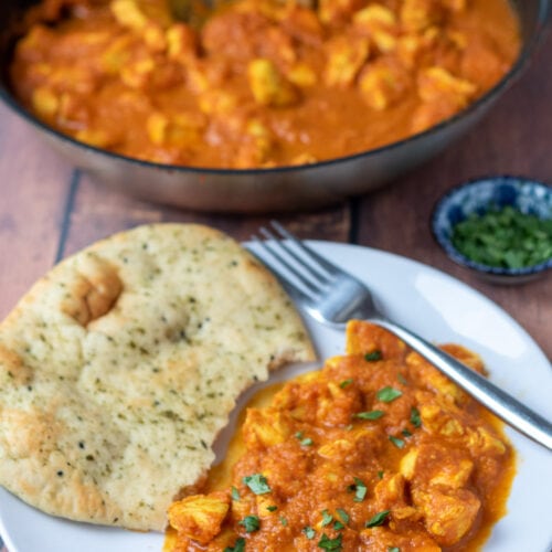 Easy chicken balti curry served on a plate with half a naan bread. Fork to the side and rest of balti curry in a pan above.
