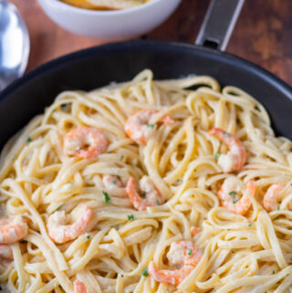 A pan of healthy creamy prawn pasta with a bowl of sliced garlic bread above.