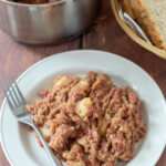 Easy corned beef stovies served on a plate with a fork to the side. Sliced bread in a basked and a pot above.