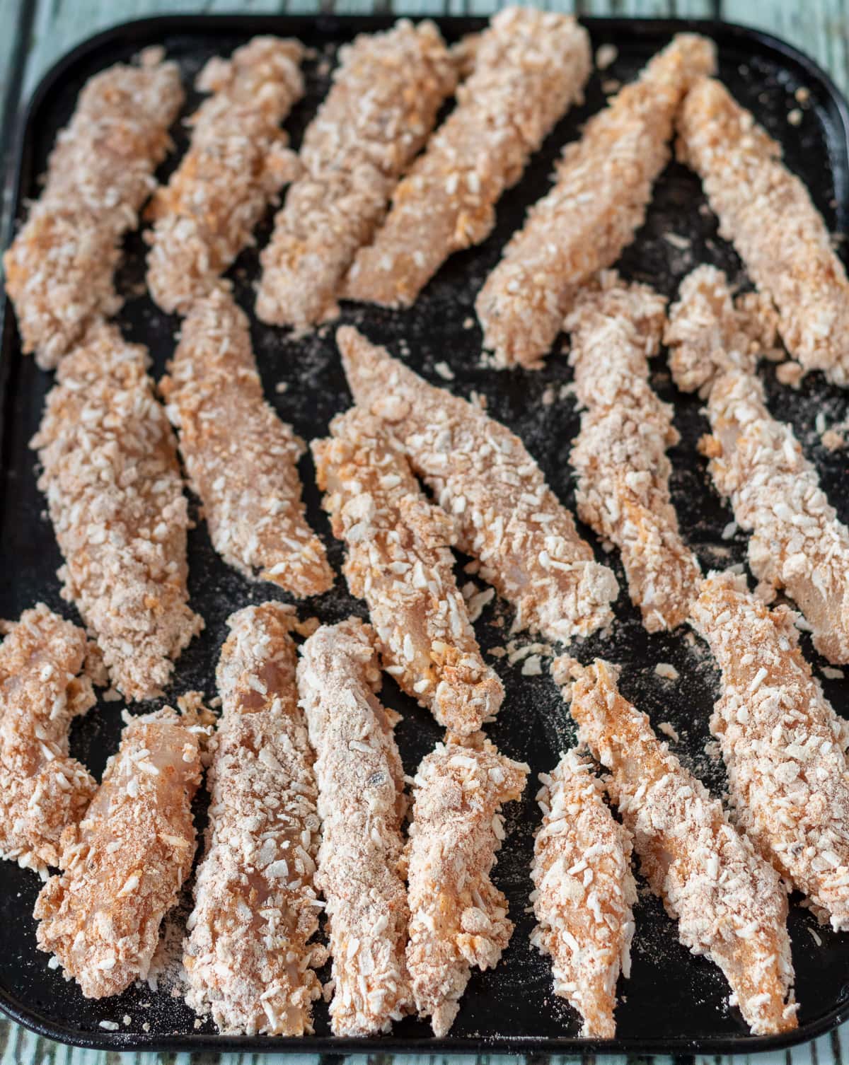 Chicken tenders coated in breadcrumb mix on a baking tray.