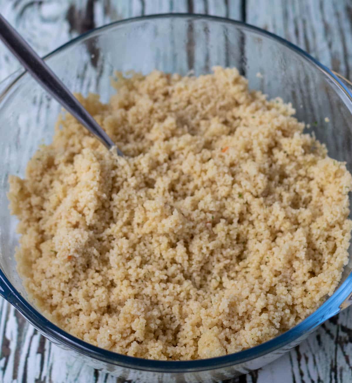 Couscous fluffed up in a large bowl using a fork.
