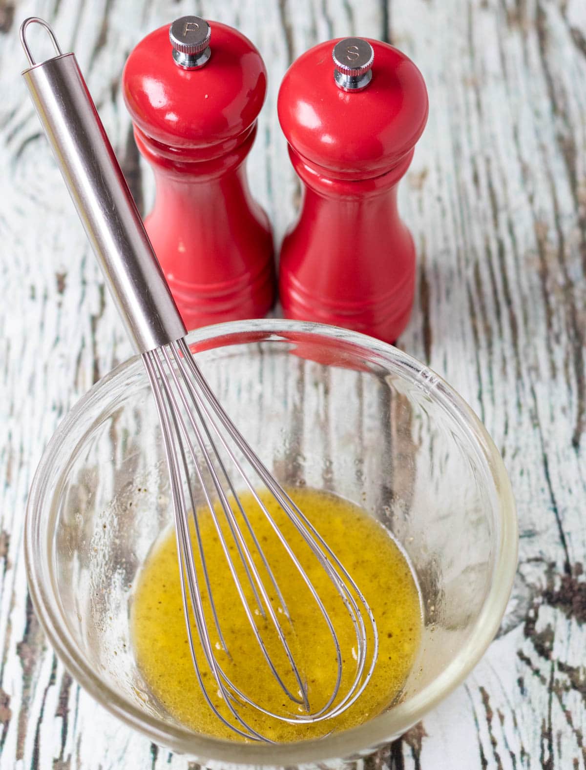 Lemon dressing in a small Pyrex bowl with a whisk in and salt and pepper cellars in the background.