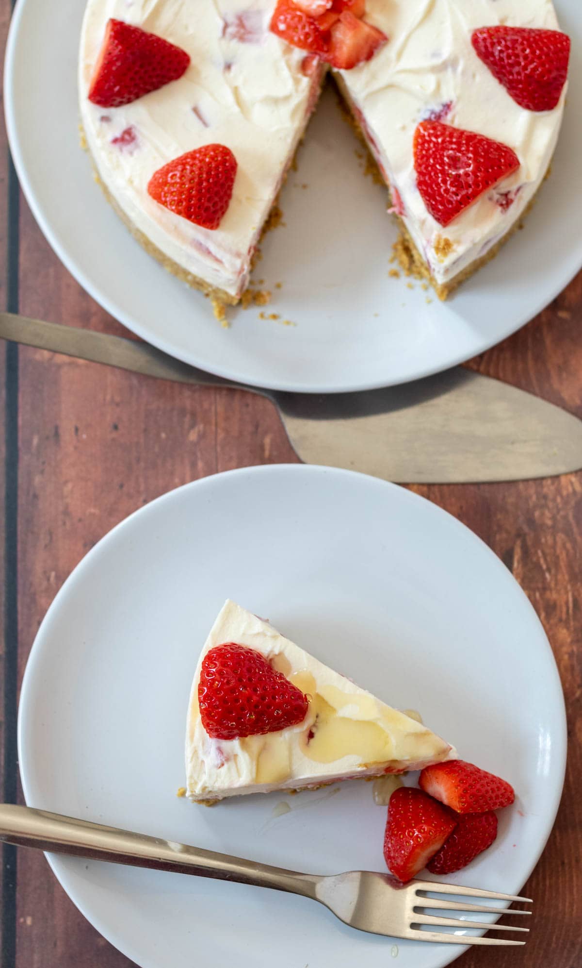 Overhead view of a slice of easy no-bake strawberry cheesecake on a plate. Rest of the cheesecut uncut on a plate above with a cake slice in between.
