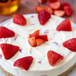 Easy no-bake strawberry cheesecake on a plate. A pile of chopped strawberries and jar of honey behind.