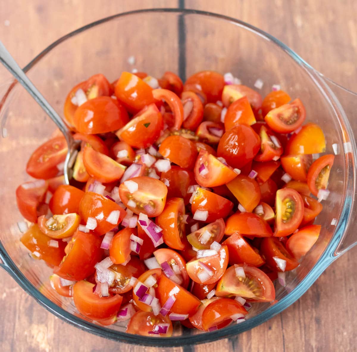 Quartered cherry tomatoes and chopped red onion in a small Pyrex glass bowl.
