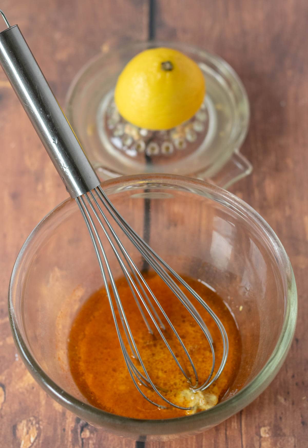 Whisk in bowl with dressing ingredients and lemon juicer in the background.