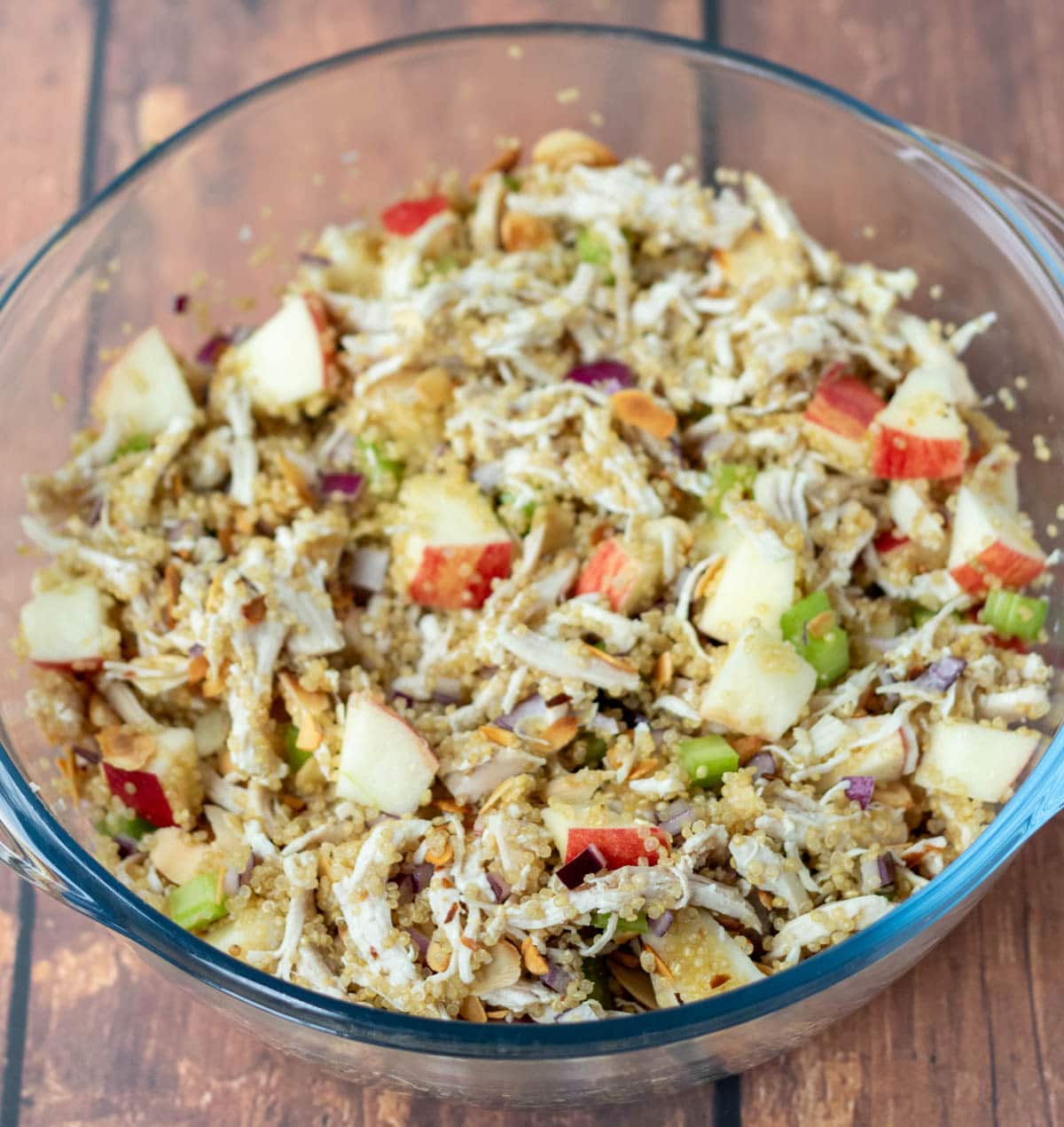 Quinoa, chicken, celery, onion, apples and almonds combined in a large glass bowl.