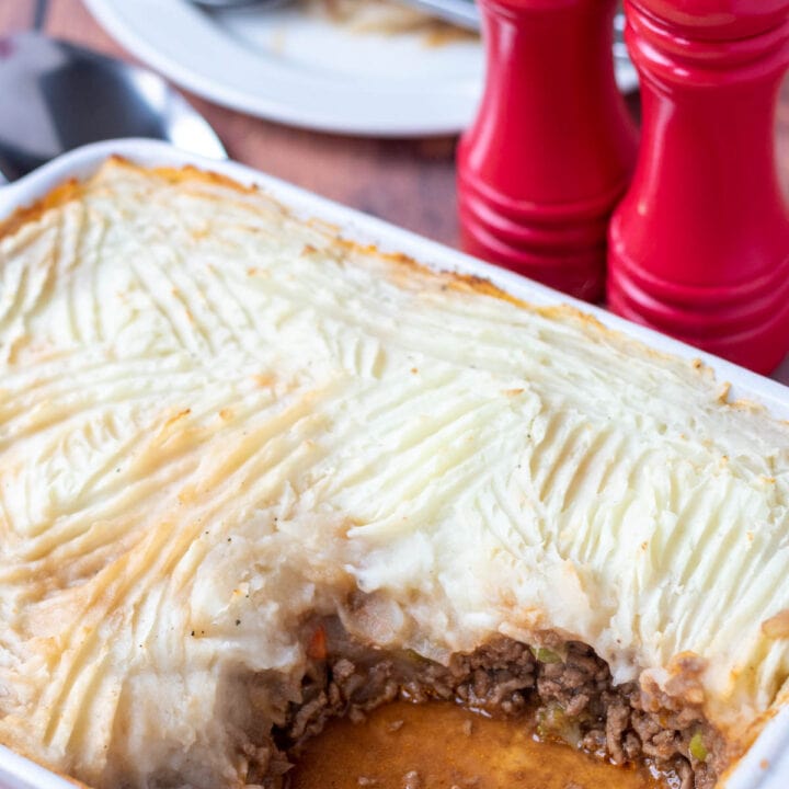 Easy shepherds pie with frozen vegetables served in a casserole dish with a portion removed. Portion on a plate in the background with salt and pepper cellars beside.