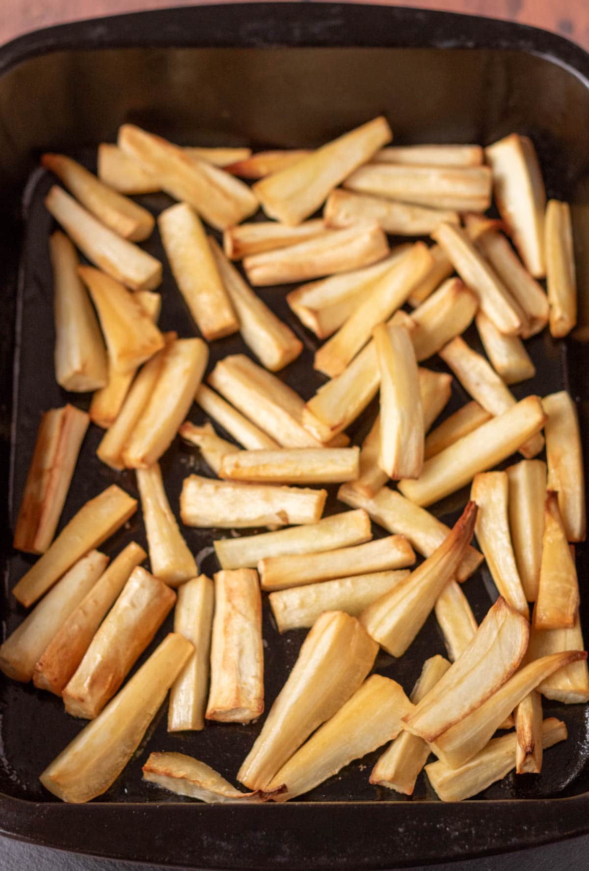 Honey glazed parsnips that have been roasted until browed and crisp in a roasting tin.