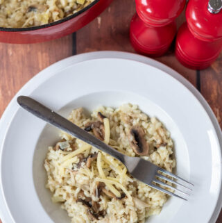Overhead view of a large dinner bowl with leftover turkey risotto served in. Fork laid over the top. Above rest of the risotto in a large casserole pot.