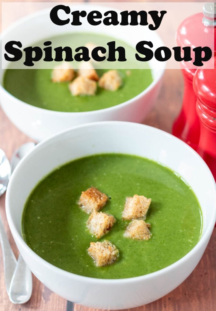 Two bowls of creamy spinach soup. One above another. Garnished with croutons. Salt and pepper cellars to the right. Soup spoons to the left. Pin title text overlay at top.