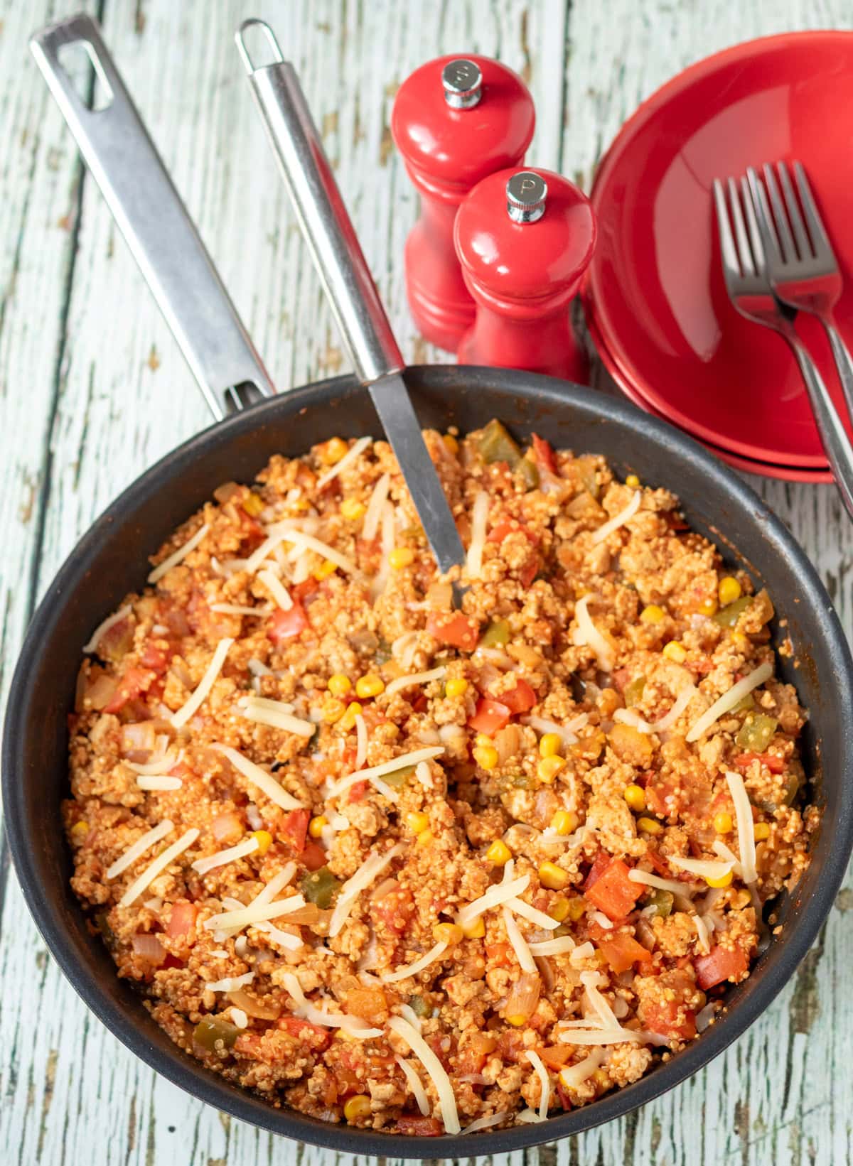 Overhead view of a pan of chicken and quinoa with a serving spoon in. Salt and pepper cellers to the top right alongside serving bowls.