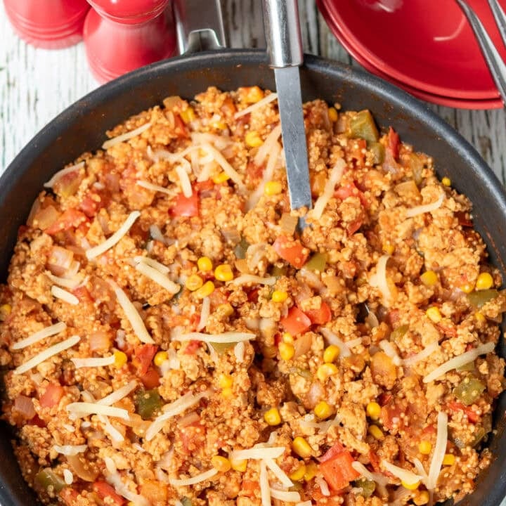 Overhead view of one pan chicken and quinoa cooked and in a large deep pan, ready to serve with a serving spoon in. Salt and pepper cellars and serving bowls with forks in above.