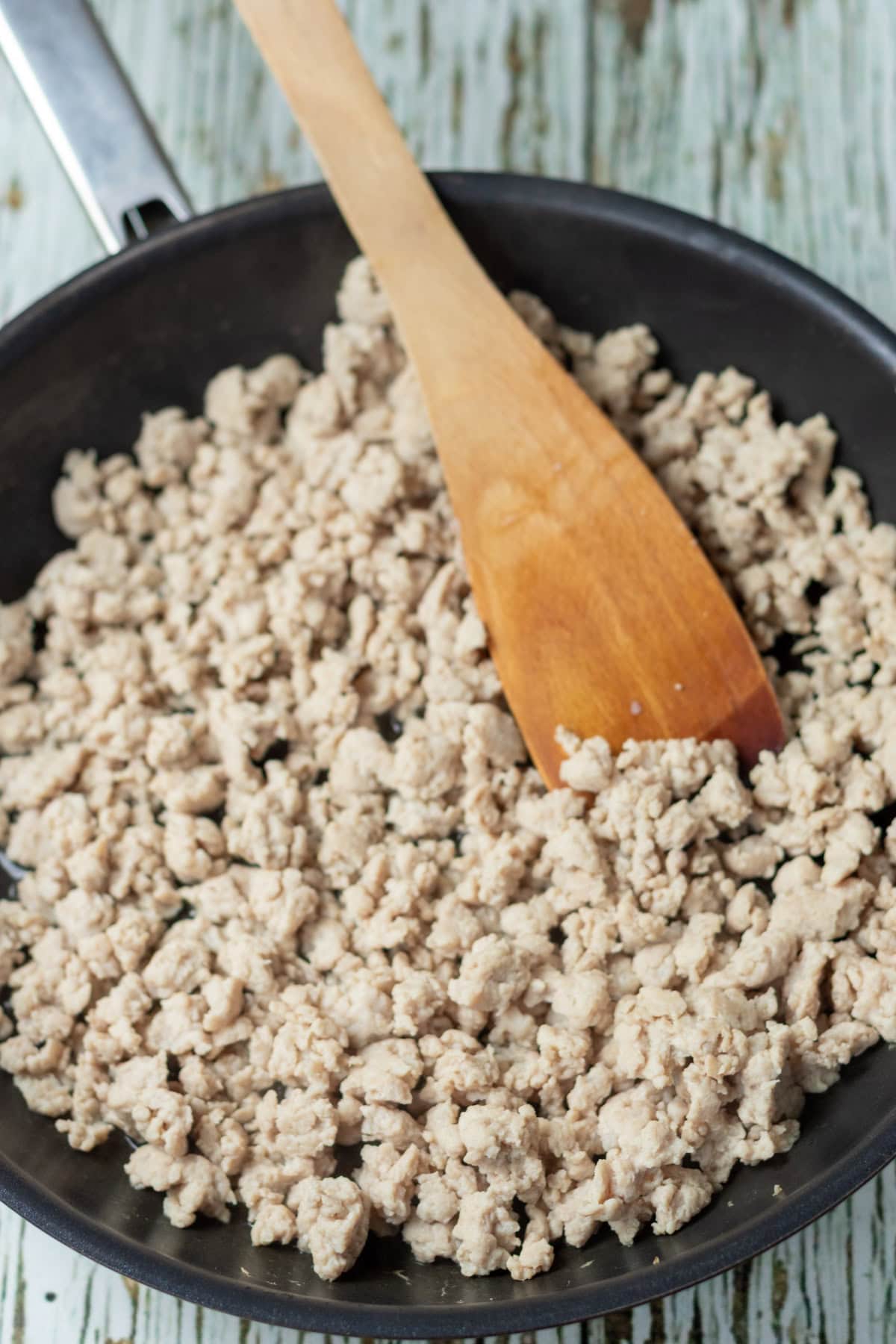 Browned chicken mince in a large deep pan with a wooden spatula.