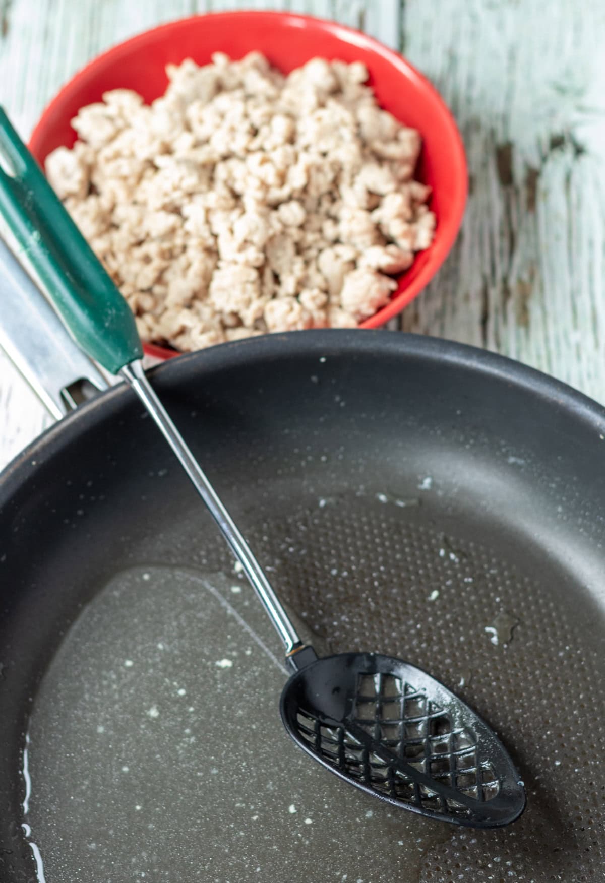 Chicken mince in a bowl above a pan with chicken juices in and a slotted spoon.