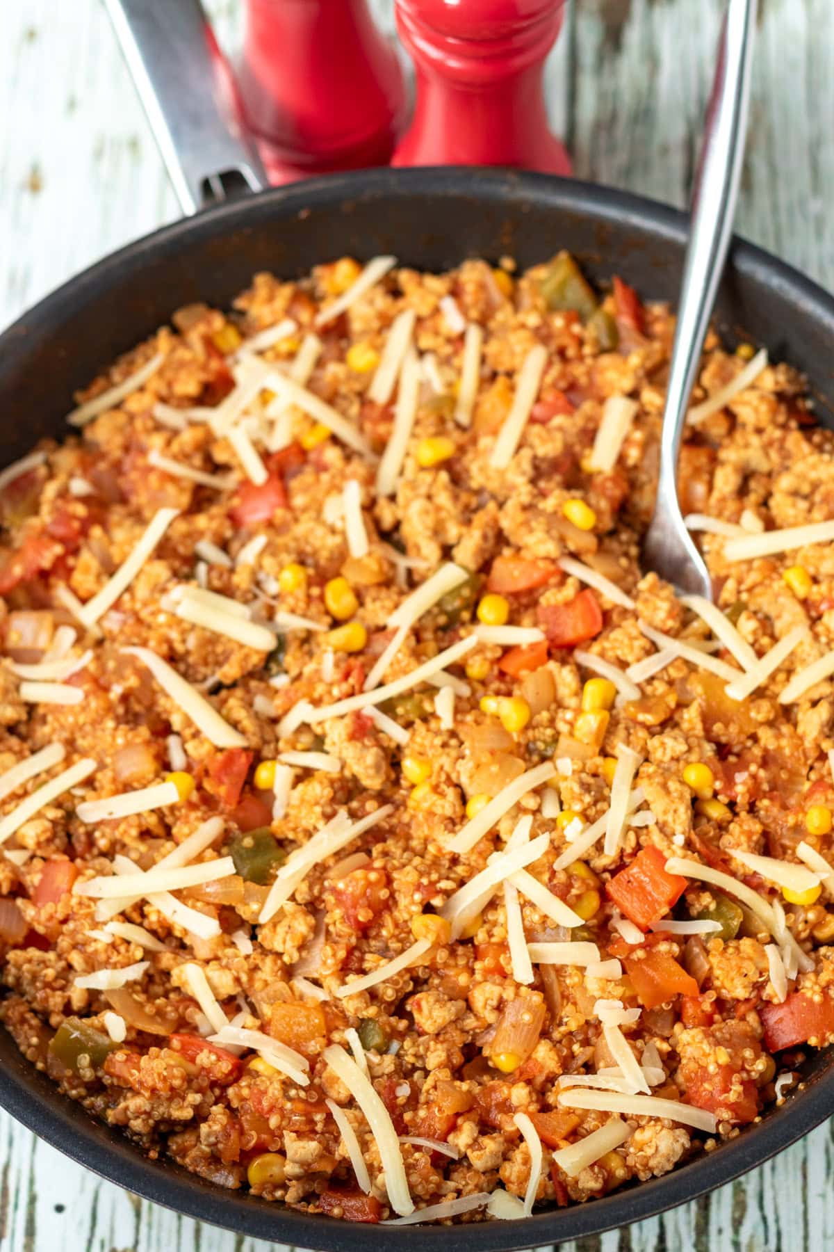 Cooked one pan chicken and quinoa in a pan resting with grated cheese over the top and a serving spoon.