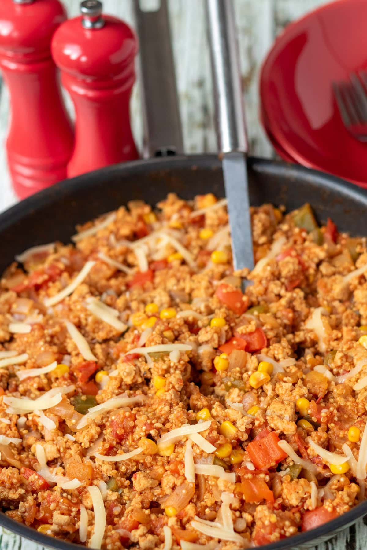 Close up view of a pan of chicken and quinoa with a serving spoon in. Above the pan there are salt and pepper cellars and bowls for serving.