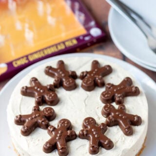 Easy no-bake gingerbread cheesecake on a plate decorated with chocolate gingerbread biscuits. In the background to the left the empty package that contained the chocolate gingerbread biscuits and to the right two plates with dessert forks on.