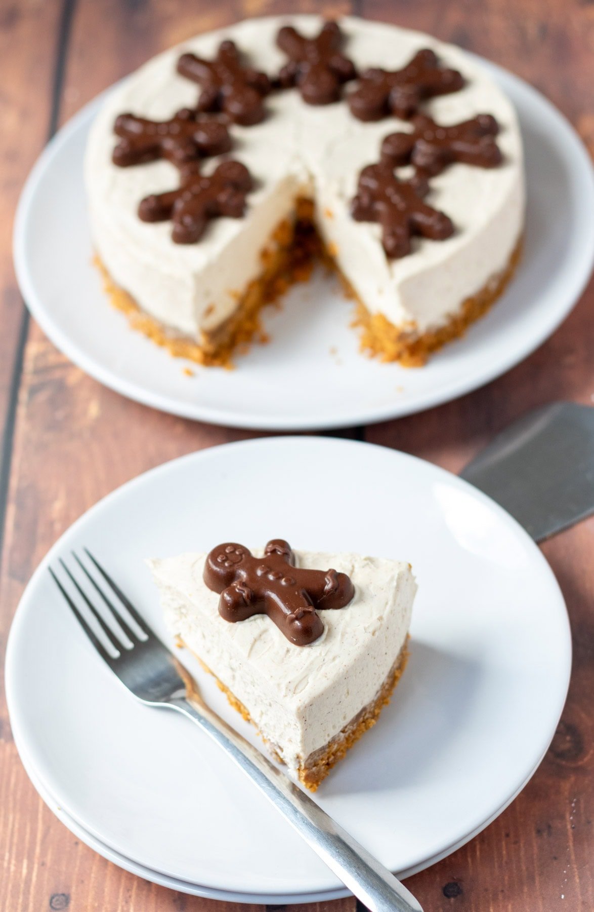 A slice of no bake gingerbread cheesecake on a plate with a dessert fork to the side at bottom. Rest of cheesecake with the slice removed on a plate at the top.