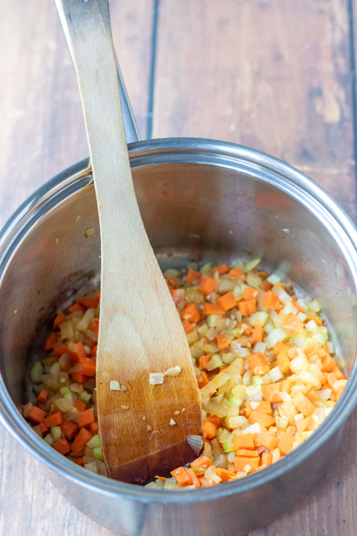 Onion, garlic, celery and carrot cooked in a large saucepan with a wooden spatula in.