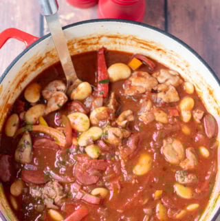 Overhead view of one pot spanish chicken and chorizo stew in a large casserole pot with a serving spoon in. Salt and pepper cellars at the top.